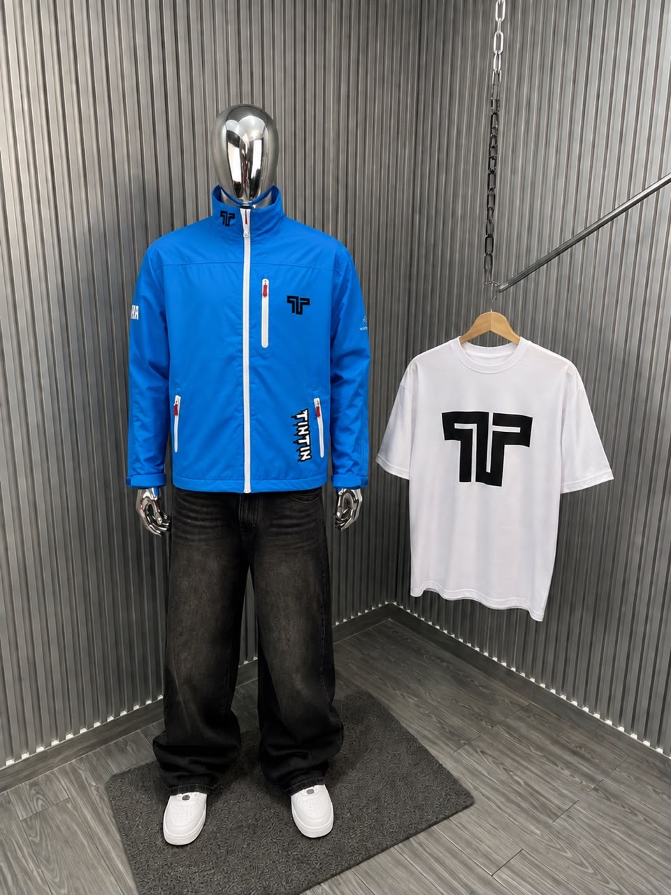 Bright blue Apex Jacket displayed on a mannequin with black jeans and a white T-shirt featuring a bold logo.