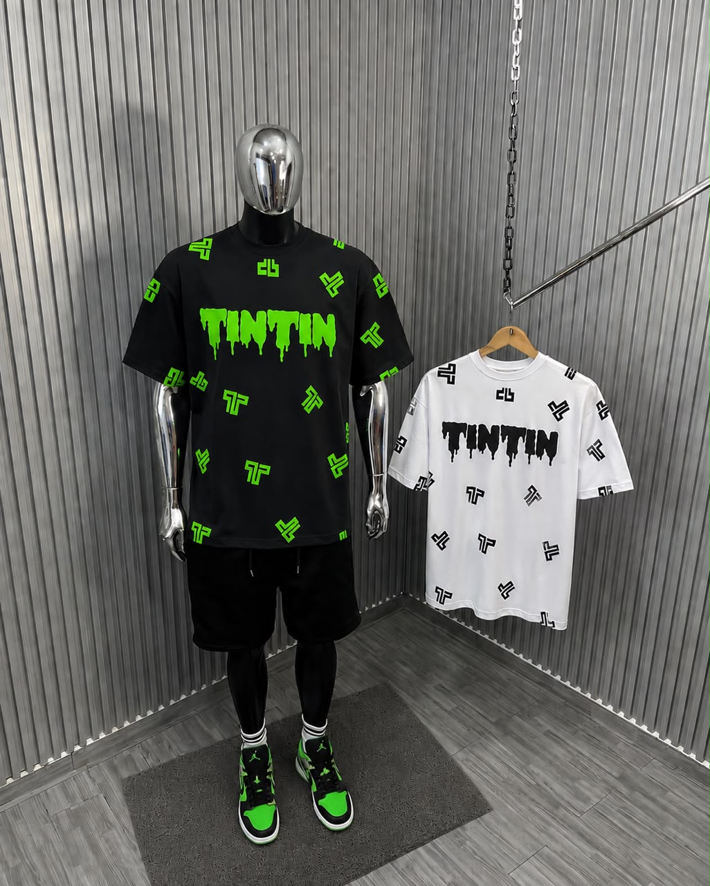 Two graphic t-shirts, one black with green accents and one white, displayed on a mannequin and hanger against a metallic backdrop.